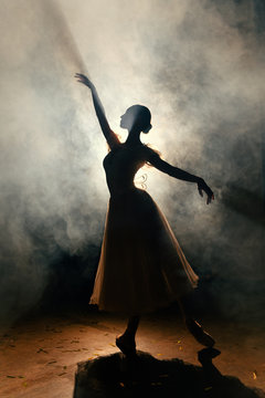 Ballerina in dress stretching on scene in darkness