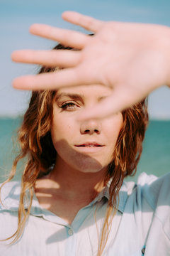 Close up portrait of a young woman putting her hand up to block the sun from her face.