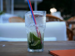 A glass of cold Mojito with ice is on the table on the summer veranda of the cafe. The glass with the tube is covered with droplets of condensate. Drink on a hot summer day.