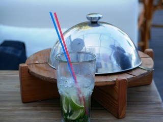 A glass of cold Mojito with ice is on the table on the summer veranda of the cafe. The glass with the tube is covered with droplets of condensate. Drink on a hot summer day.