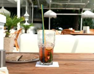 Two glasses of cold mojitos and an iced strawberry cocktail sit on a table on the cafe's summer veranda. Glasses with a tube covered with droplets of condensate. Refreshing drinks on a hot summer day.