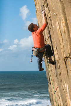 Guy climbing on rock hill near seashore