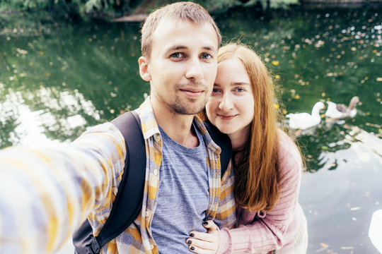 Young married couple makes selfie on the background of a lake with ducks. Cute family content for social networks.