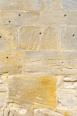 idyllische, schön restaurierte Sandsteinmauer eines historischen Gebäudes aus gelbem Sandstein mit verschiedener  Oberflächenstruktur, manche Steine haben Auswaschungen und Löcher, wie Schusslöcher