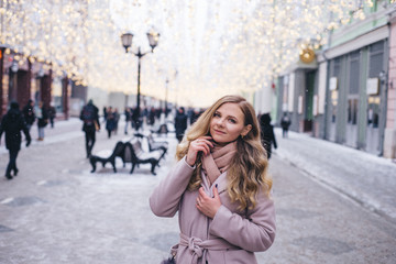 A young woman walks at Christmas in the square near the decorated Christmas trees. Candy is a lollipop in the form of a heart.