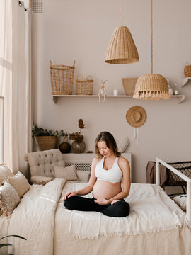 Happy young woman in expectancy sitting on bed