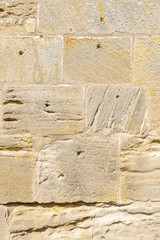 idyllische, schön restaurierte Sandsteinmauer eines historischen Gebäudes aus gelbem Sandstein mit verschiedener  Oberflächenstruktur, manche Steine haben Auswaschungen und Löcher, wie Schusslöcher