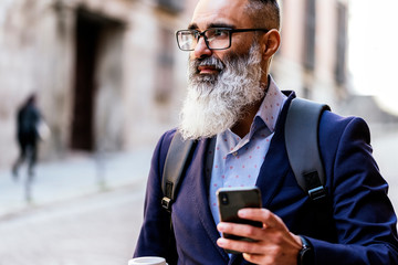 Handsome senior businessman using his phone in the street