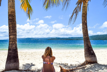 Woman sitting on white beach between two palms in front of beautiful ocean