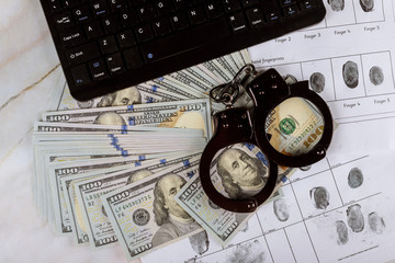 Cyber crime legal law police handcuffs on a hundred dollar bills with computer keyboard technology of fingerprint on paper