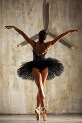 Full body portrait. Russian ballerina in a black dancing suit is posing in dark studio