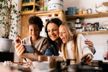 Woman with smartphone near amazed children in kitchen