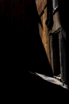 A shaft of late afternoon sunlight creates strong shadows on the sidewalk and side of a building in Grasse, France.
