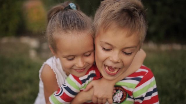 Two fun little kids, a boy and a girl, are playing with soap bubbles in the Park at sunset. Little brother and sister blowing bubbles on the grass in the Park.