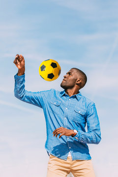 Black man playing with a yellow soccer ball outdoors