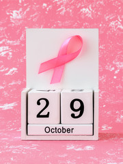 Pink ribbon of breast cancer awareness on a white wooden perpetual calendar with date 29 october. International breast cancer awareness month.