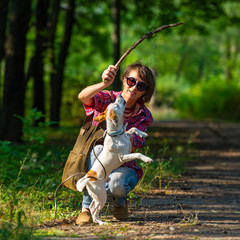 Pretty woman in glasses is training a dog in a city park in the morning.