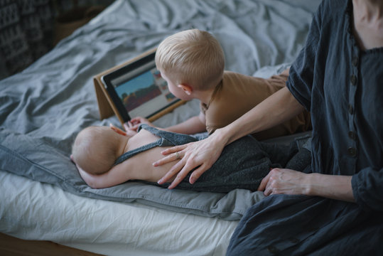 Young children play in an electronic tablet next to their mother
