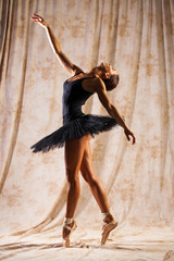 Full body portrait. Russian ballerina in a black dancing suit is posing in dark studio