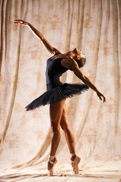 Fototapeta Full body portrait. Russian ballerina in a black dancing suit is posing in dark studio