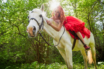 Girl in beautiful red dress on white horse in Park or forest. Photo shoot models and fashion
