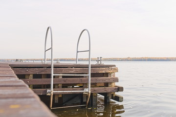 A metal staircase on the edge of an empty wooden river pier descends to the water. Harbor for parking a yacht or boat.