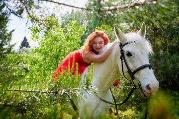 Girl in beautiful red dress on white horse in Park or forest. Photo shoot models and fashion