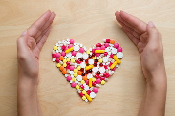 A heart shape laid out of multi-colored tablets on a table, covered with hands on both sides
