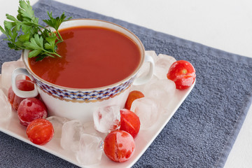 Summer cold tomato soup (gazpacho). Ice and frozen tomatoes on a plate. Gray napkin, white background.