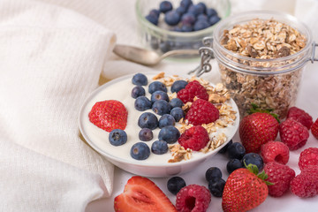 Yogurt in white bowl with strawberries and blueberries on white background.
