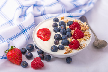 Yogurt in white bowl with strawberries and blueberries on white background.
