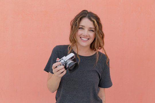 Portrait of woman with camera against blank wall.
