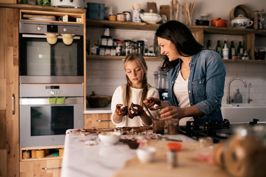 Child with dough and cocoa near happy woman in kitchen