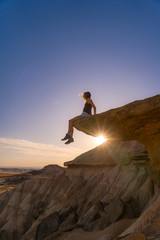 Lifestyle session of a young blonde on top of a stone sitting in the desert at a sunset in Bardenas Reales, Spain...