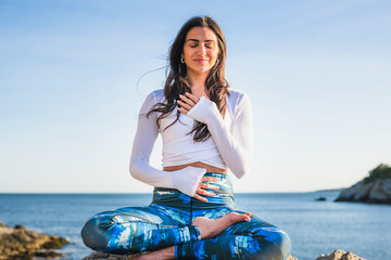Young woman doing yoga on the rocks at golden hour