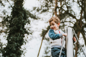 Portrait of boy on climbing frame against blurred background of trees