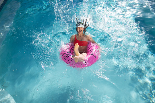 Laughing young woman jumping into pool with inner tube