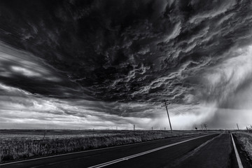 Heavy storm and cloud sky over road and farm fields, black and white