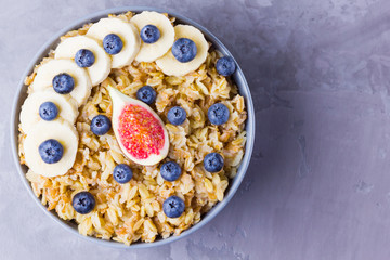 Healthy breakfast. Oatmeal with blueberries, banana and figs. Oatmeal with fruits and berries in a bowl. Cooked oatmeal on cement background. Copy space