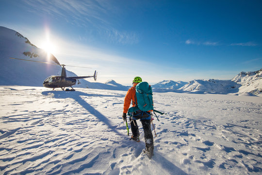 Climber approaches a helicopter, landed on a glacier for a luxury tour