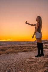 A young woman hitchhiking in the desert at a sunset