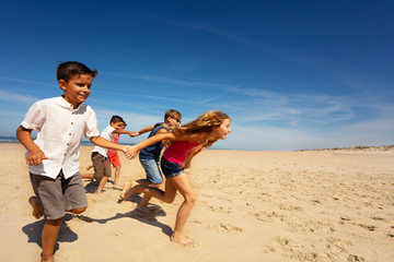 Group of kids run fast for fun on sea sand beach