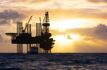 Offshore drilling platform during sunrise with work vessel
