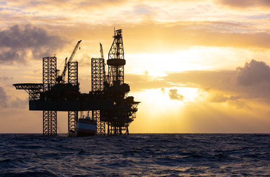 Offshore drilling platform during sunrise with work vessel