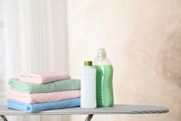 Stack of clean towels and laundry liquid on ironing board, copy space