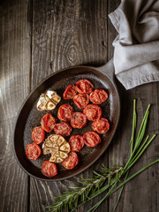 Roasted cherry tomatoes with garlic in black pan with grey linen. Overhead shot..