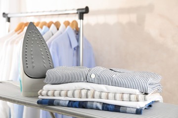 Iron and stack of shirts on ironing board, space for text