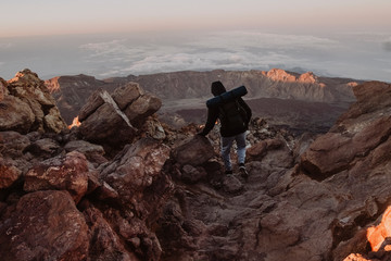 A male hiker walks on trail over the clouds at sunrise Teide