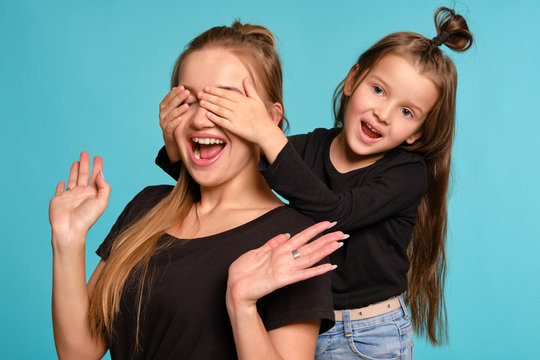 Mom and daughter with a funny hairstyles, dressed in black shirts and blue denim jeans are posing against a blue studio background. Close-up shot.