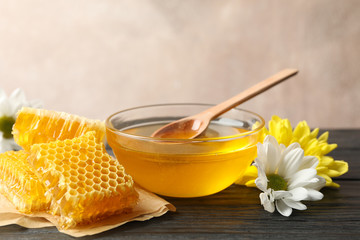 Bowl with honey, honeycombs and flowers on wooden background, copy space